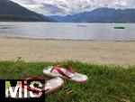 20.06.2020, Lago Maggiore Italien, Ansicht auf den See. Badeschlappen liegen einsam im Gras am Sandstrand.