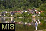 04.05.2023, Hopfensee in Bayern, Der Hopfensee bei Fssen im Allgu, Eine Rentnerin steht am See, die Huser der Promenade spiegeln sich im ruhigem Wasser an dem sonnigen Sonntag-Morgen. (Modelreleased)