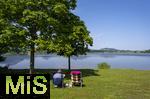 04.05.2023, Hopfensee in Bayern, Der Hopfensee bei Fssen im Allgu, Urlauber sitzen am See auf ihren Campingsthlen und geniessen die Aussicht.