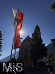 31.07.2025, Meran in Sdtirol, Italien. Ortsteil Dorf Tirol,  Landesflagge von Sdtirol weht an der Kirche. Die Landesflagge von Sdtirol mit dem Sdtiroler Wappen in der Mitte zeigt einen doppelkpfigen, schwarzen Adler auf goldenem Grund, der auch als Wenzeladler bekannt ist, und einen roten Adler auf weiem Grund, der das Tiroler Wappen darstellt. Die Flagge ist ein Symbol fr die Autonomie und Identitt Sdtirols innerhalb Italiens. Pfarrkirche Hl. Johannes der Tufer