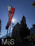 31.07.2025, Meran in Sdtirol, Italien. Ortsteil Dorf Tirol,  Landesflagge von Sdtirol weht an der Kirche. Die Landesflagge von Sdtirol mit dem Sdtiroler Wappen in der Mitte zeigt einen doppelkpfigen, schwarzen Adler auf goldenem Grund, der auch als Wenzeladler bekannt ist, und einen roten Adler auf weiem Grund, der das Tiroler Wappen darstellt. Die Flagge ist ein Symbol fr die Autonomie und Identitt Sdtirols innerhalb Italiens. Pfarrkirche Hl. Johannes der Tufer