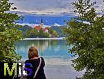 03.09.2025, Bled, Slowenien, Der Bleder See, auch Veldeser See oder Felder See, slowenisch Blejsko jezero, ist ein See in der slowenischen Region Oberkrain (Gorenjska) beim Kurort Bled. Blick  auf die Insel Blejski Otok mit der bekannten Marienkirche mitten im See. Besucherin steht am See.